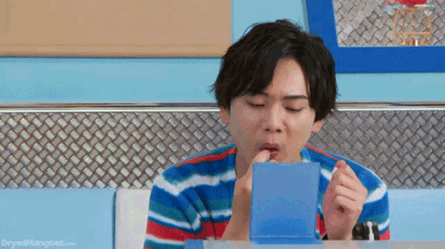 a man in a striped shirt is sitting at a table eating something from a blue box