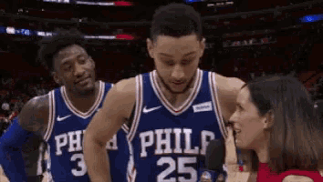 two philadelphia 76ers players are talking to a reporter on the court