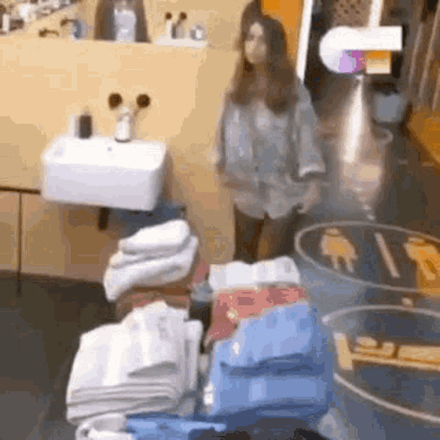 a woman is standing in a bathroom next to a sink and a table filled with towels .