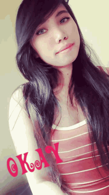 a girl with long black hair is wearing a striped tank top and the word okay is on her arm