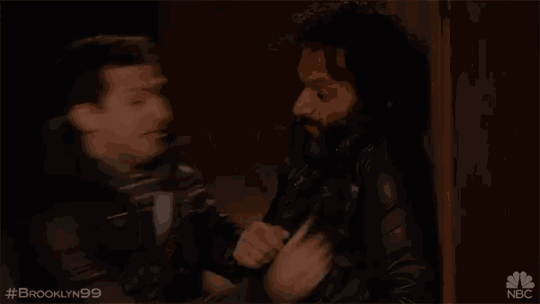 two men are standing next to each other in a dark room . one of the men is wearing a black leather jacket .
