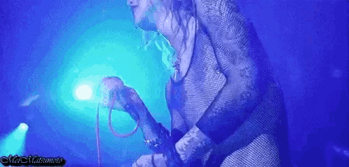 a person is singing into a microphone in a dark room with a blue light behind them