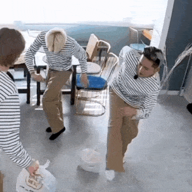 three men in striped shirts are dancing in a room while one of them is holding a bag .