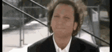 a man with curly hair is wearing a suit and tie and making a funny face .