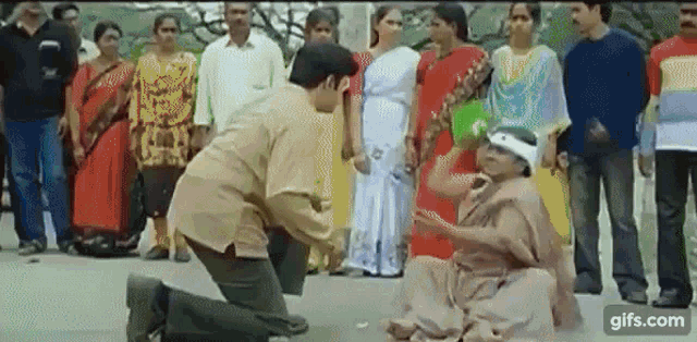 a man is kneeling down next to a woman sitting on the ground in front of a crowd .
