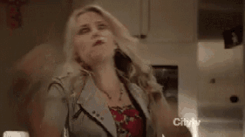 a woman is making a funny face while holding her fist in the air in a kitchen .