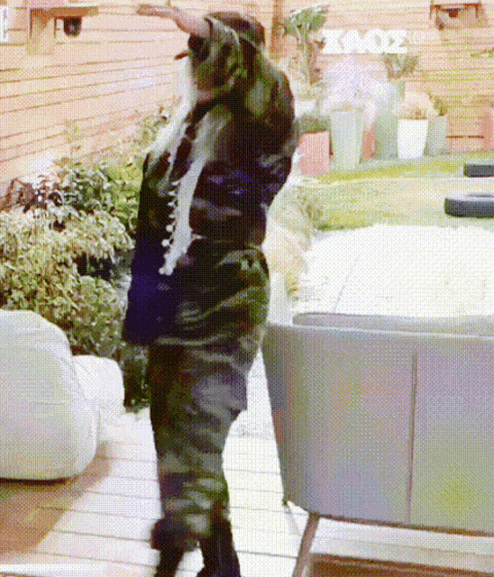a woman in a camouflage outfit is dancing in front of a wall that says kmdz