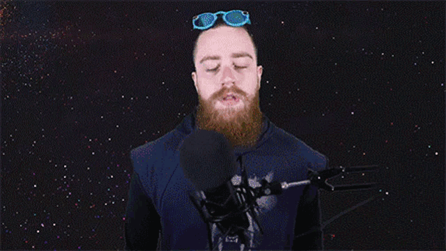 a man with a beard wearing neon sunglasses is talking into a microphone in a purple and green background .
