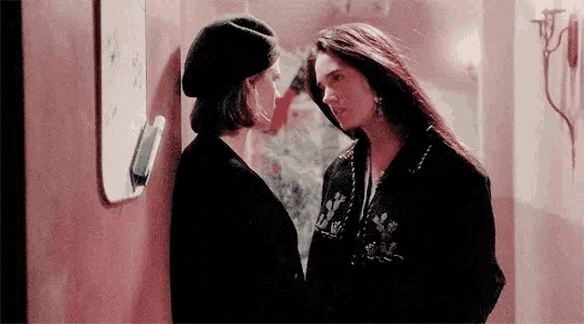 two women are standing next to each other in a hallway .