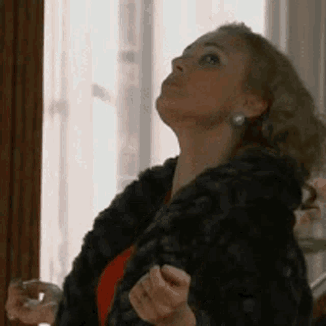 a woman in a fur coat is looking up while holding a glass .