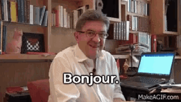 a man is sitting at a desk with a laptop and says bonjour