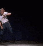 a man in a white shirt and blue jeans is dancing on a stage in front of a blue curtain .