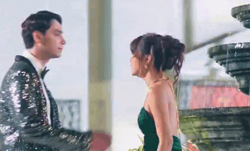 a man in a tuxedo and a woman in a green dress are standing next to each other and kissing .