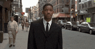 a man in a suit and tie stands on a street in front of a store that says weiss