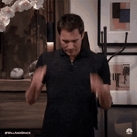 a man in a black shirt is standing in a living room with his hands in his pockets .