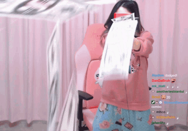 a woman in a pink sweater is holding a piece of paper in front of her face while sitting in a pink chair