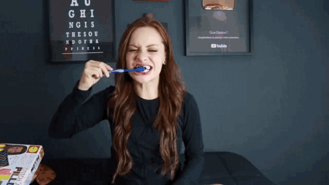 a woman is brushing her teeth with a blue toothbrush in front of a sign that says ao ghi ngis