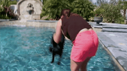 a woman in pink shorts is standing in a pool with a black dog