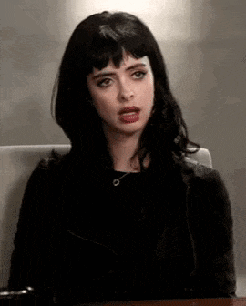 a woman with black hair and bangs is sitting at a table making a funny face .
