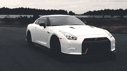 a white sports car is driving down a road with the words art of the automobile on the bottom right