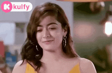a woman wearing a yellow tank top and earrings is making a funny face .