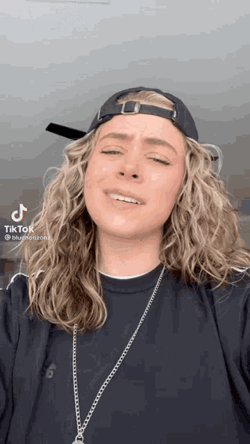 a woman wearing a hat and a necklace is making a face .