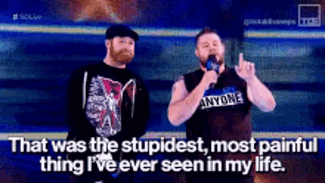 two men are standing next to each other on a stage talking into microphones .