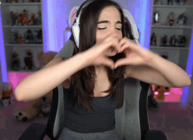 a woman wearing headphones making a heart with her hands