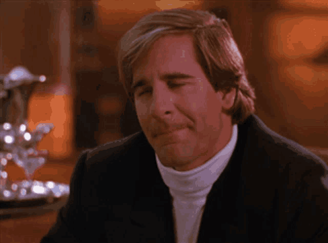 a man in a suit and white turtleneck is making a face