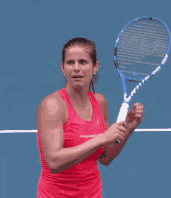 a woman in a red tank top is raising her arms in the air on a tennis court .