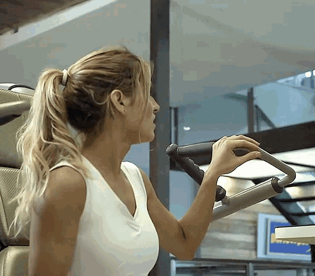 a woman in a white tank top holds onto a handle of a machine