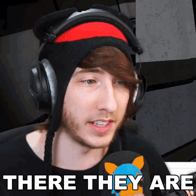 a man wearing headphones and a hat with the words there they are behind him