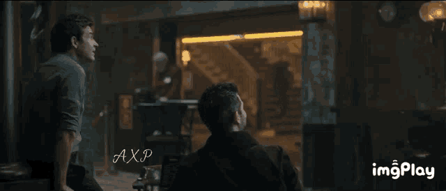 two men are sitting next to each other in a dark room with the letters axp on the bottom