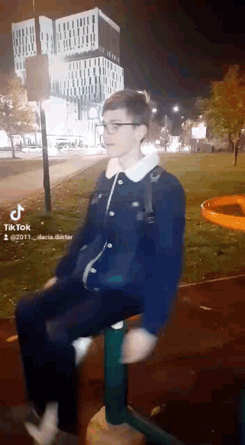 a man in a blue jacket is sitting on a seesaw at night .