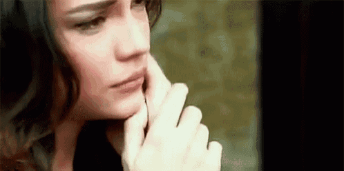 a woman is touching her face with her hand and looking at the camera .