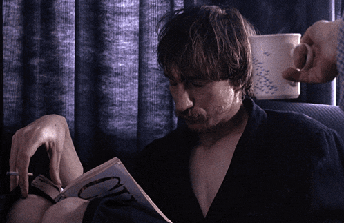 a man smoking a cigarette while reading a book with the letter o on it