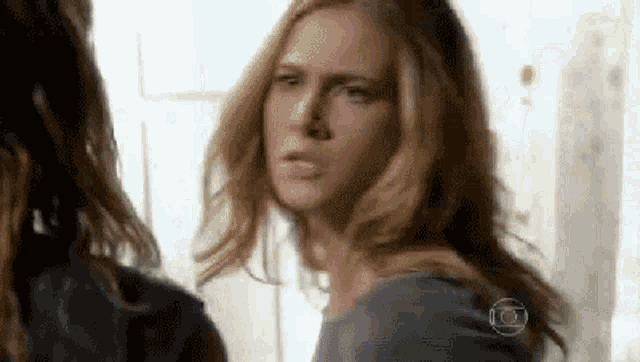a woman with long blonde hair is making a funny face while talking to another woman .
