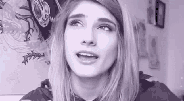 a close up of a woman 's face in a black and white photo with a painting in the background .