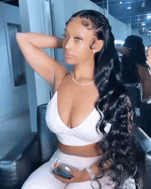a woman in a white crop top is sitting in a chair with her hand on her head