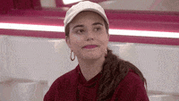 a woman wearing a hat and earrings is sitting at a table in a diner .
