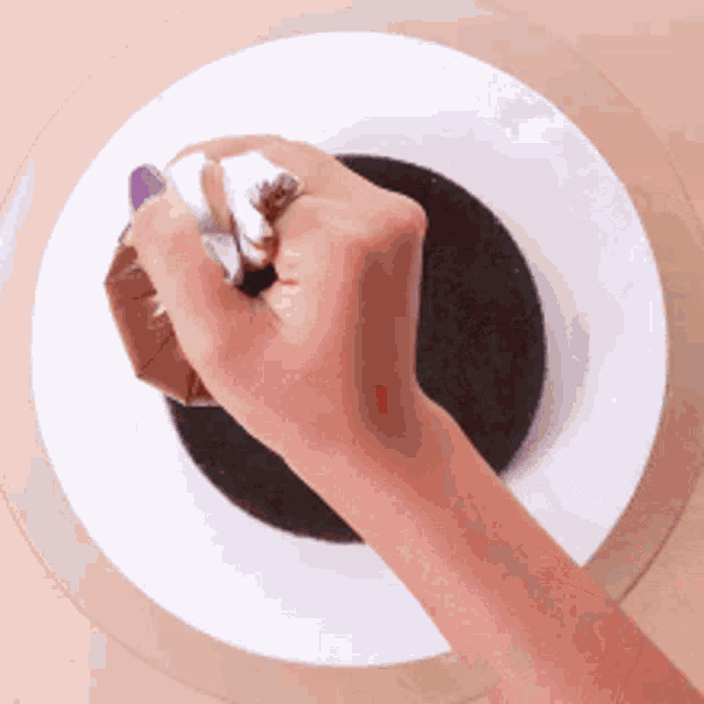 a person 's hand is holding a piece of chocolate over a white plate .