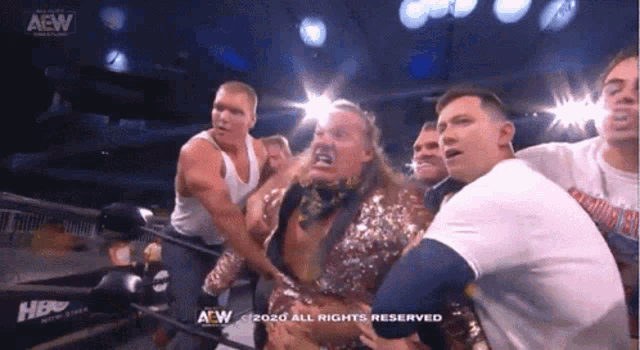 a group of men are standing around a wrestler in a ring with a aew logo in the background