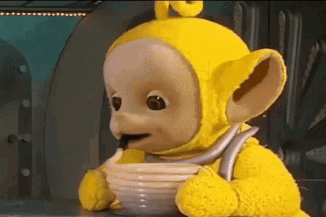 a yellow teletubbies stuffed animal is holding a bowl of food .