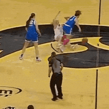 a basketball game is being played on a court with a referee standing in the middle .