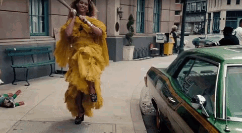 a woman in a yellow dress is holding a bat and walking down the street .