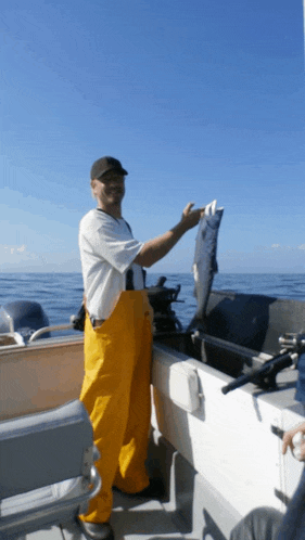 a man in yellow overalls is standing on a boat holding up a fish