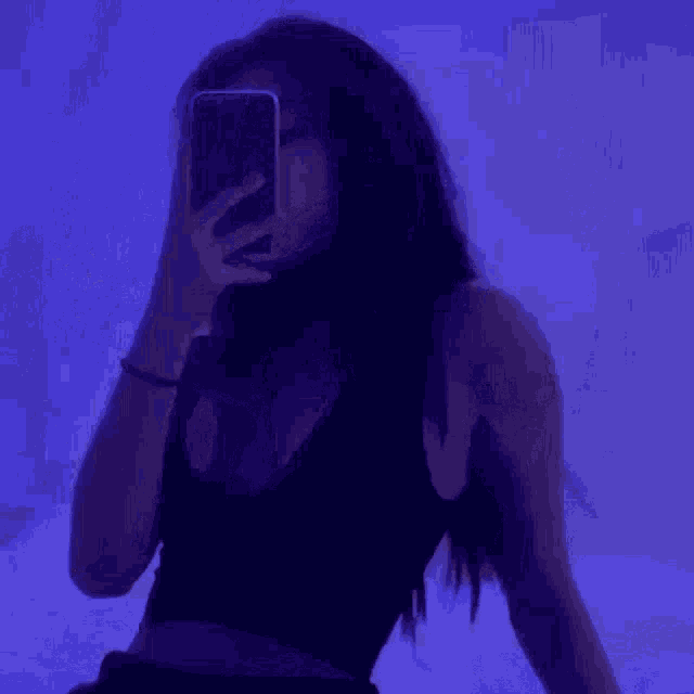 a woman is taking a selfie with her cell phone in front of a blue wall .