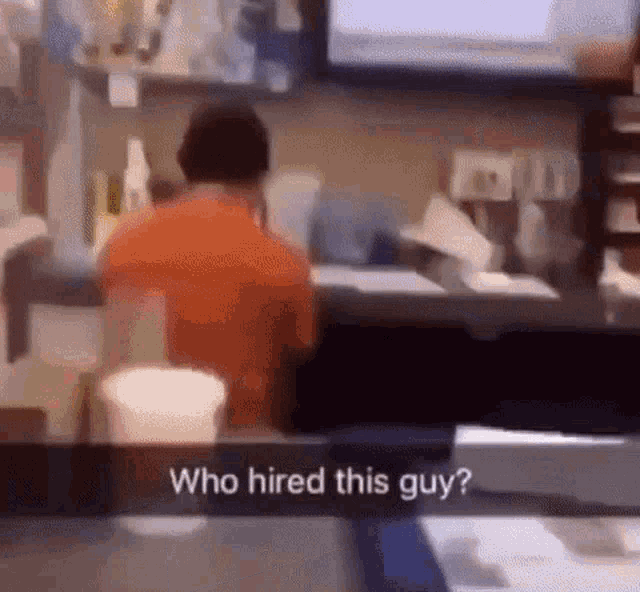 a blurred image of a man sitting at a counter with the caption who hired this guy .