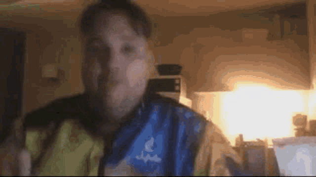 a man in a blue and yellow jacket is sitting in a kitchen eating food .