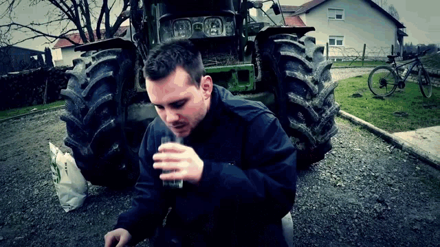 a man drinks a glass of water in front of a tractor